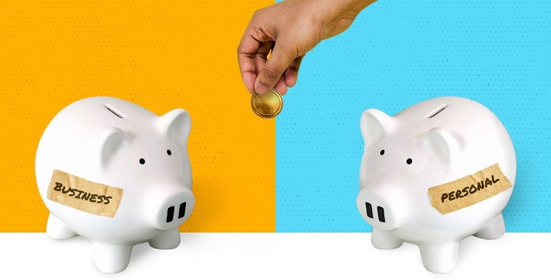 Two piggy banks, one labeled personal one labeled business with a hand holding a coin in the center symbolizing the challenge of keeping these areas separate in finances.